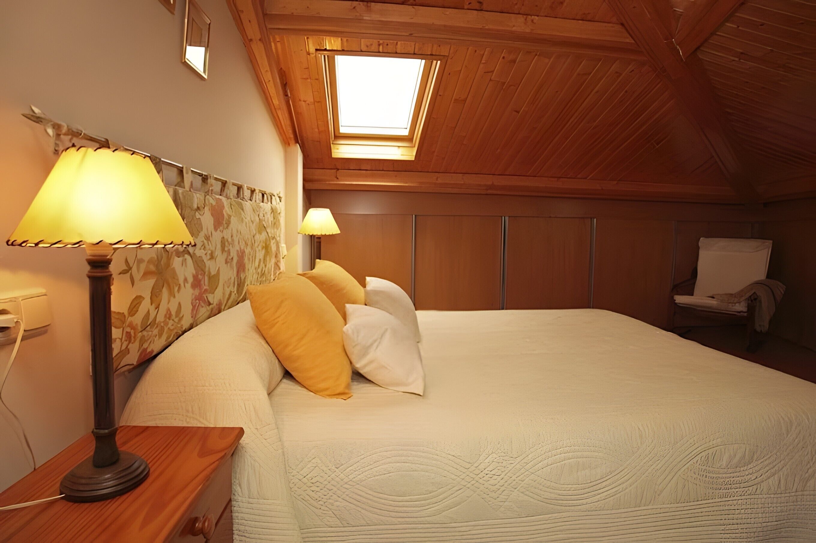 Une chambre avec un grand lit, deux lampes de chevet, un plafond en bois et une lucarne.