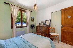 A bedroom with a bed, a dresser, a chair, a fan, and a door. - House 'Chez N E L' with Private Pool and Garrigue View (La Tour-sur-Orb)