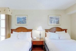 Een hotelkamer met twee bedden, een nachtkastje met een lamp en twee ingelijste foto's aan de muur.
