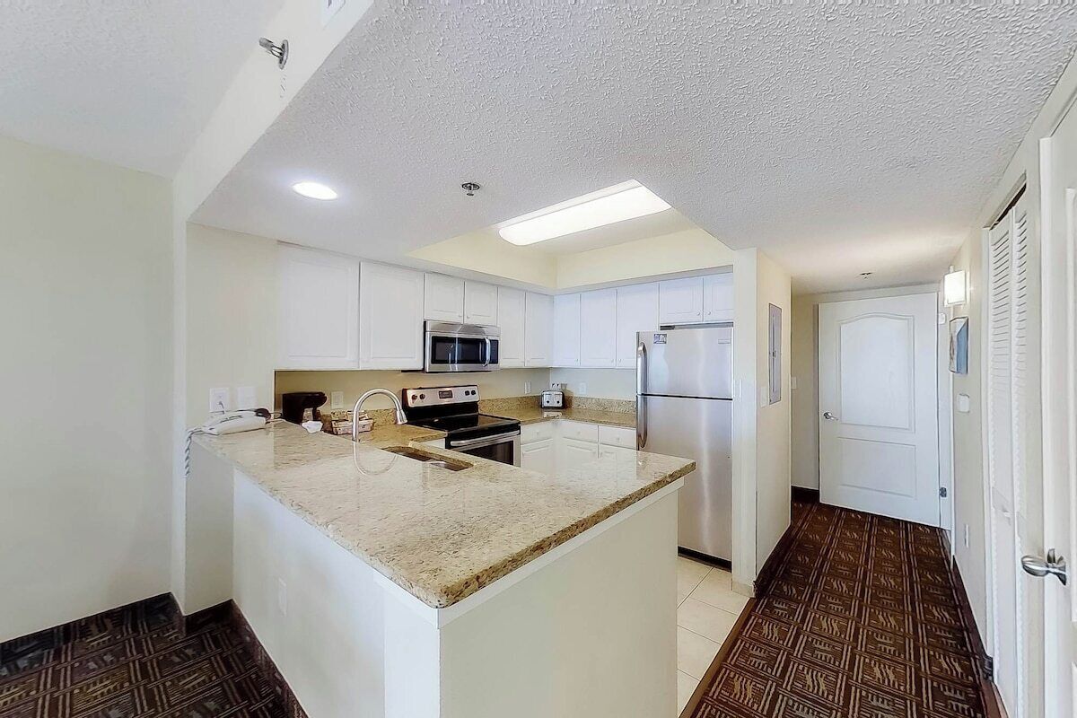 A compact kitchen with white cabinets, a central island, stainless steel appliances, and patterned flooring.