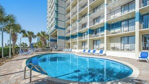 A hotel pool area with a curved pool, lounge chairs, and a multi-story building with balconies. - Carolinian Beach Resort 1830 (Myrtle Beach)