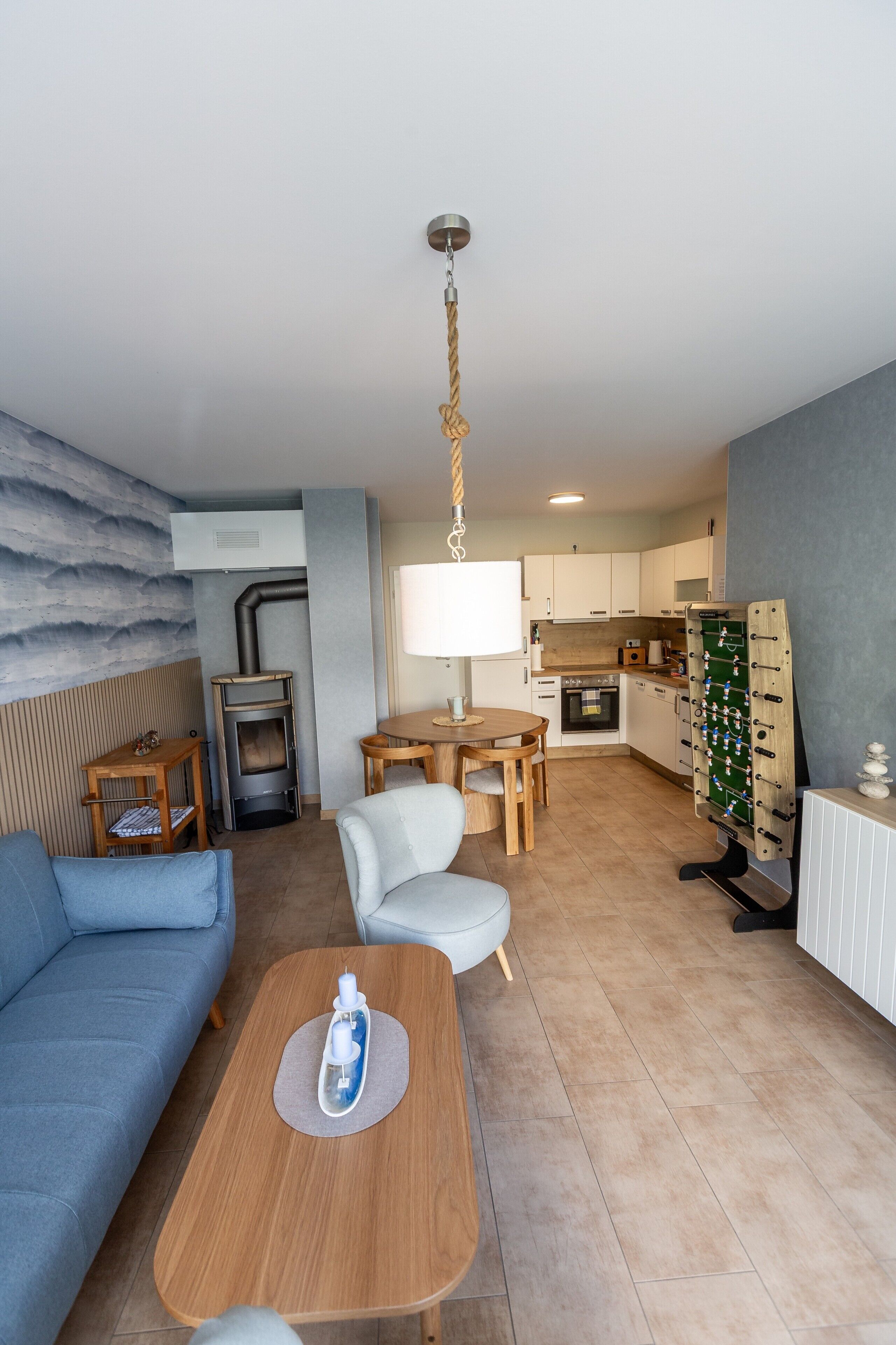 Ein modernes Wohnzimmer mit einer Couch, einem Couchtisch mit Kerzen, einem Kamin und einer Küchenzeile mit einem Kicker.