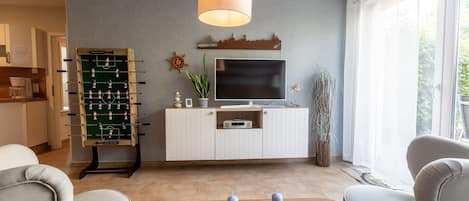 Un salon moderne doté d’un baby-foot, d’un téléviseur à écran plat et d’une grande fenêtre laissant entrer la lumière naturelle.