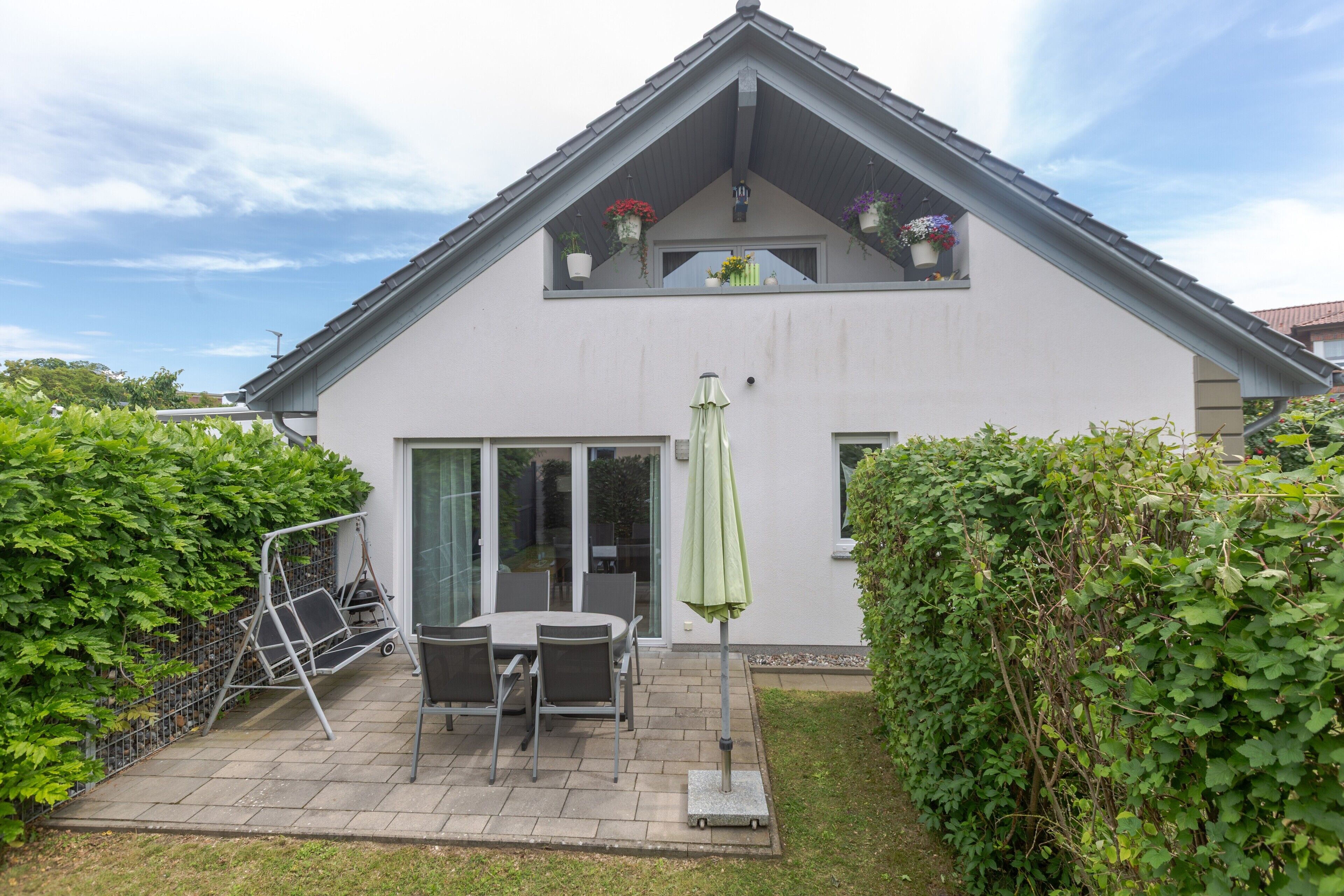 Une maison à deux étages avec un patio, une porte-fenêtre coulissante et un parasol vert.