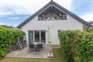 Una casa a due piani con un patio, una porta scorrevole in vetro e un ombrellone verde.