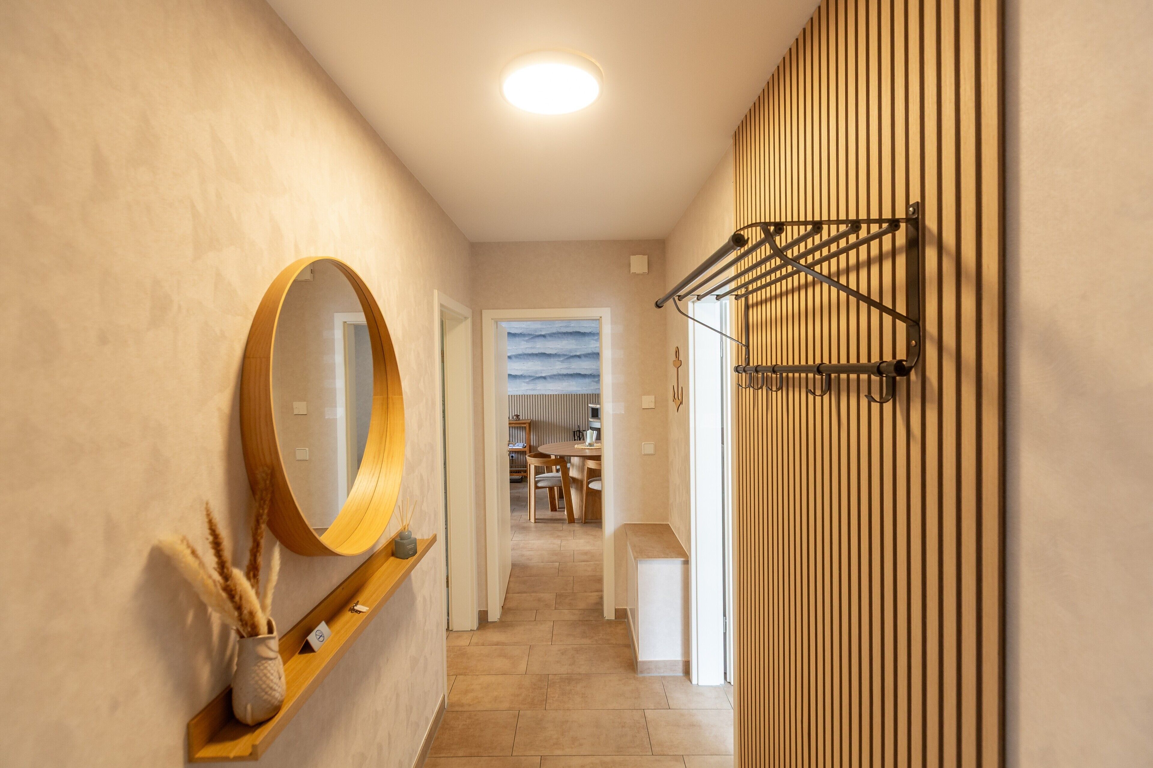 Un couloir doté d’un plancher en bois, un miroir rond sur le côté gauche et un porte-serviettes sur le côté droit.