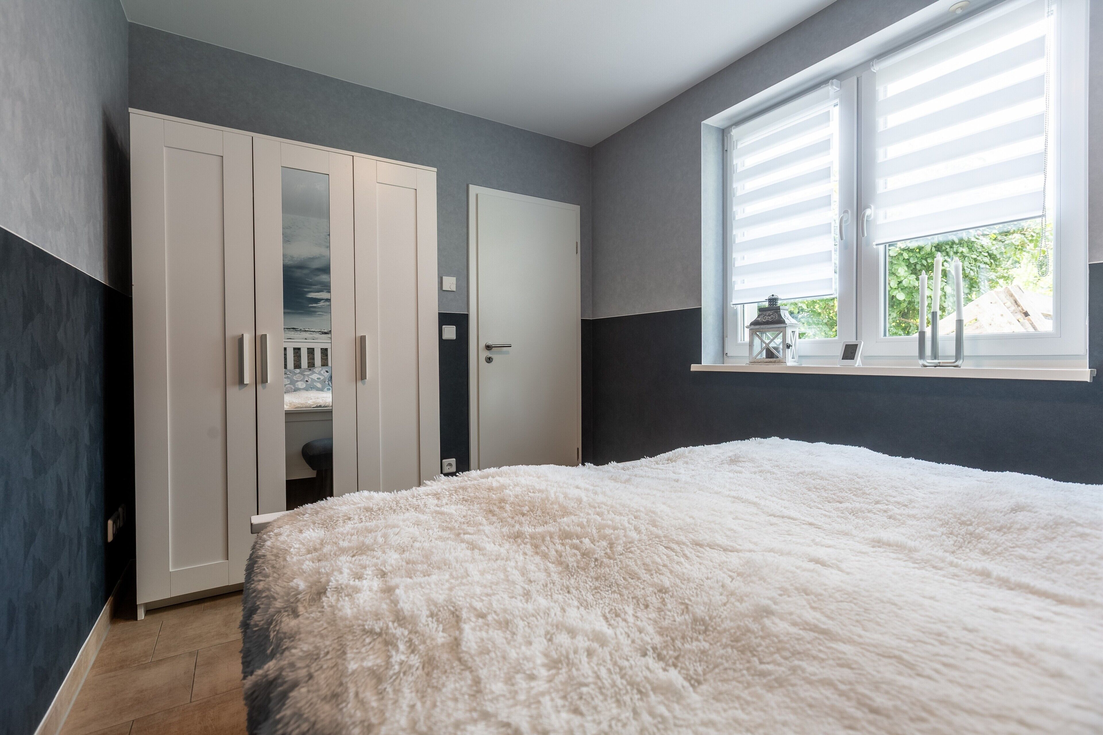 Ein Schlafzimmer mit einem großen Bett, einem Kleiderschrank, einer Tür und einem Fenster mit Jalousien.