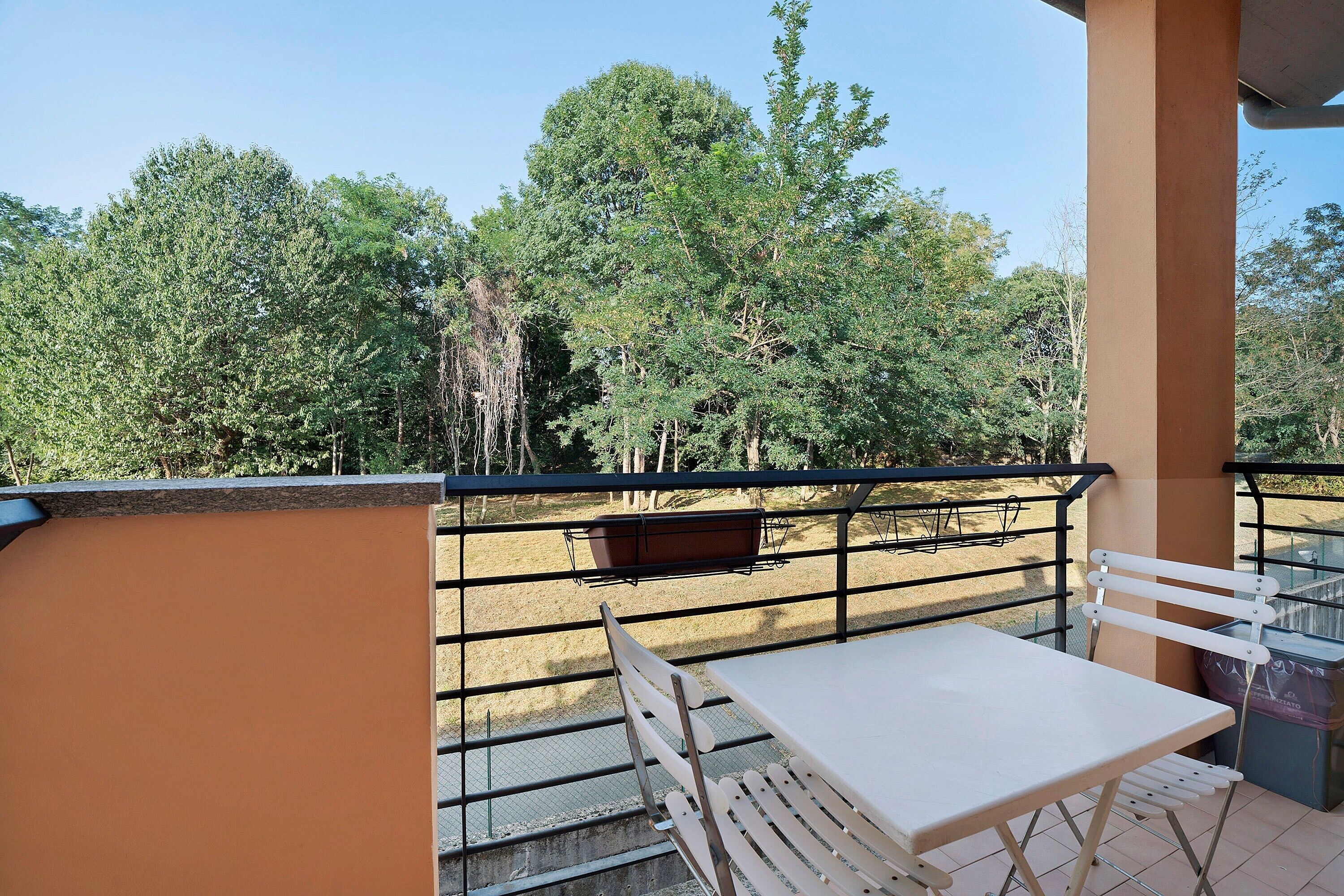 Un balcon avec une table et des chaises, une rambarde en métal et une vue sur les arbres.