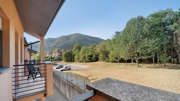 A balcony with a view of a parking area, a mountain, and a forest. - Azalea City Center Apartment with Shared Pool, Wi-Fi, and Air Conditioning (Induno Olona)
