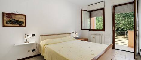 A bedroom with a bed, bedside tables, a nightstand, a window with a view, and a wall-mounted motorcycle poster.
