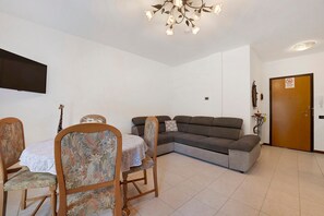 Ein Wohnzimmer mit Esstisch, Stühlen, einer Couch und einem Fernseher.