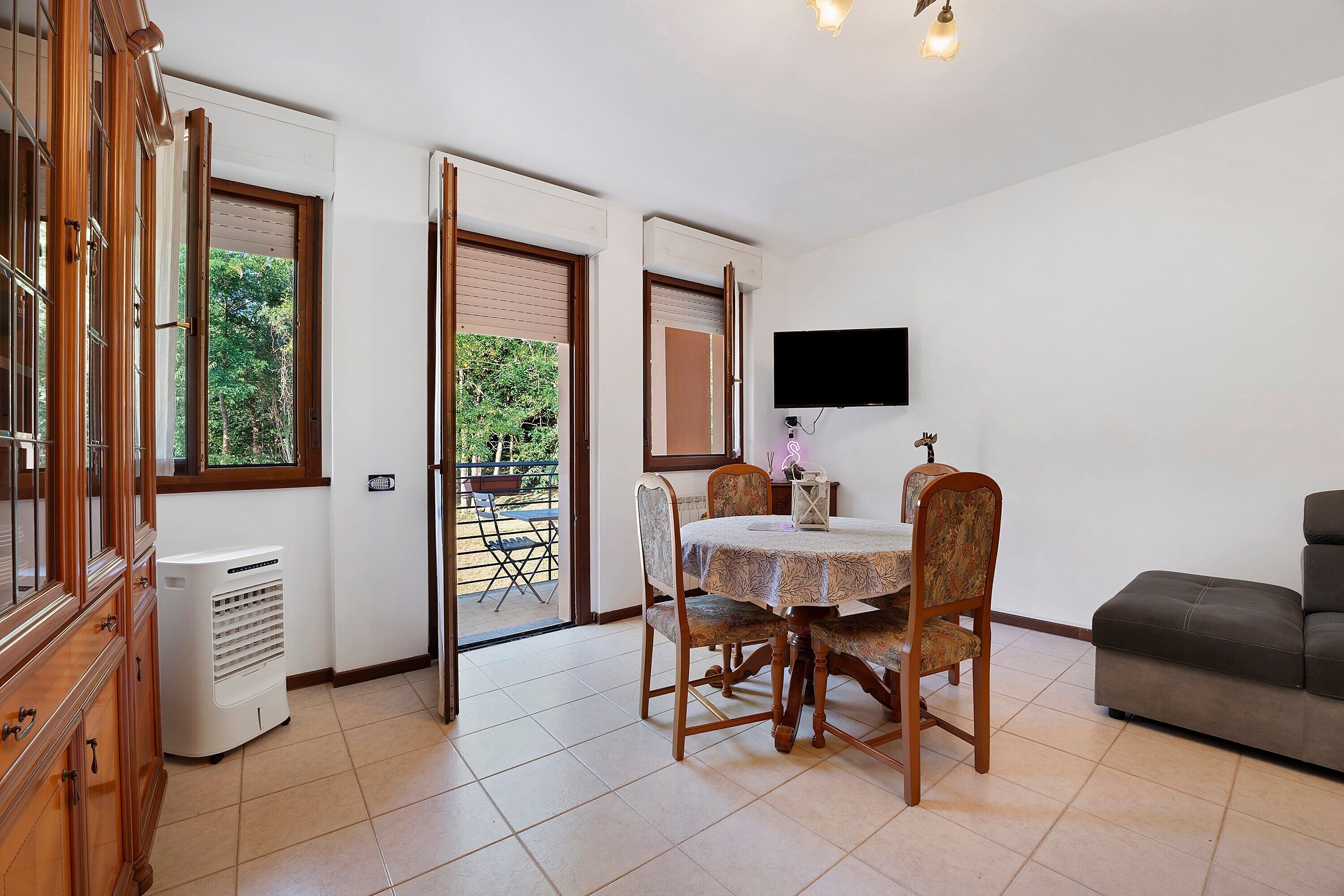 Una habitación con una mesa de comedor, sillas, un televisor montado en la pared y un sofá.