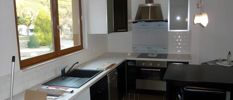 Ett modernt kök med vita skåp, en rostfri köksfläkt och ett fönster med utsikt över en trädgård.