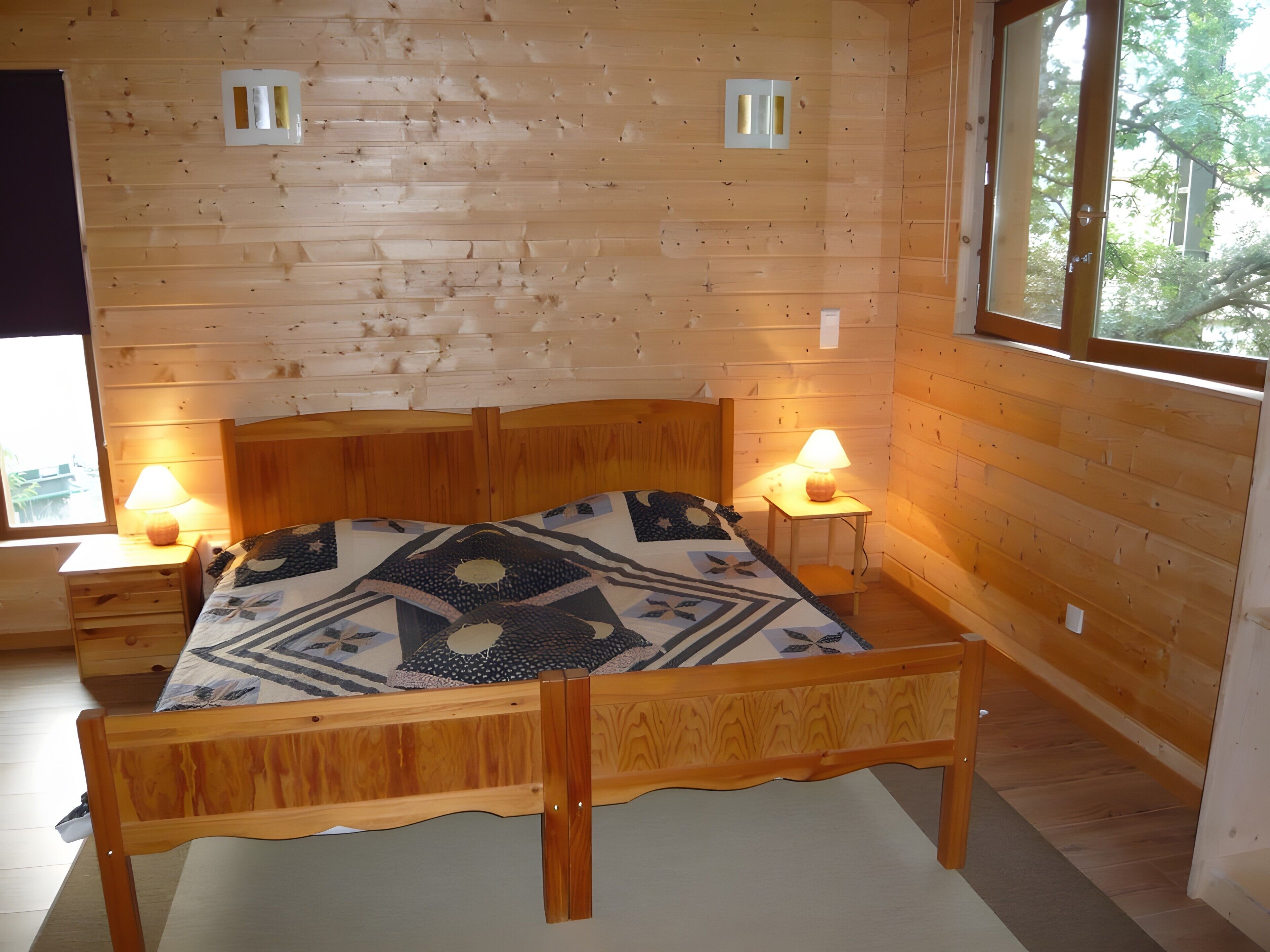 Ein Zimmer mit Holzwänden, einem Bett, zwei Nachttischlampen und einem Fenster.