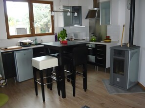Moderni keittiö, jossa on keskeinen saareke, baarituolit, sisäänrakennettu liesi ja ikkuna, josta tulee luonnonvaloa.