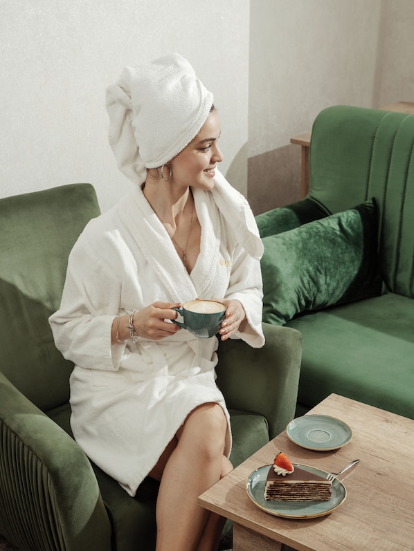 A person seated on a green sofa with a plate of food and a cup in front. - Grand Kristal Baku (Baku)