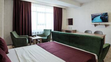 A hotel room with a bed, two chairs, a desk, a television, and a window with curtains.