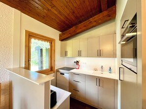 A modern kitchen with white cabinets, a wooden ceiling, and a window with a heart-patterned curtain. - Ski-in/ski-out apartment with balcony in Combloux (Combloux)