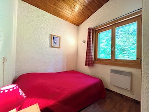 Ein kleines Zimmer mit einem Einzelbett, einem Fenster mit Blick auf Bäume und einem Wandheizkörper.