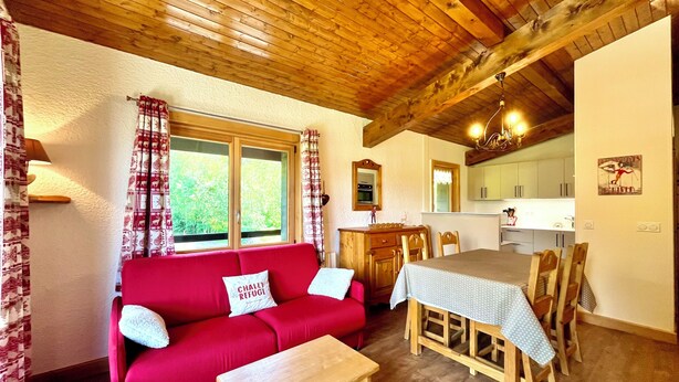 A cozy living room with a red sofa, wooden dining table, and a kitchen area with a window. - Ski-in/ski-out apartment with balcony in Combloux (Combloux)