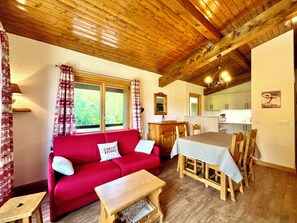 A cozy living room with a red sofa, wooden dining table, and a kitchen area with a window. - Ski-in/ski-out apartment with balcony in Combloux (Combloux)