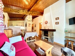 A cozy living room with a fireplace, wooden furniture, and a television. - Ski-in/ski-out apartment with balcony in Combloux (Combloux)