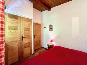 A bedroom with a wooden wardrobe, a bedside table with a lamp, and a red bedspread. - Ski-in/ski-out apartment with balcony in Combloux (Combloux)