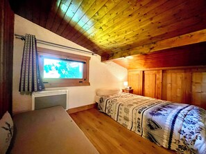 A small, cozy room with a single bed, a window with curtains, a bedside table with a lamp, and a wooden ceiling. - Ski-in/ski-out apartment with balcony in Combloux (Combloux)