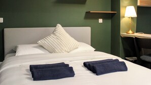 A neatly made bed with two folded towels, a white pillow, and a textured white pillow on a green wall. - Cozy Studio in Central Paris (16m²) (Paris)