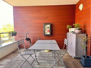 A patio with a metal table and chairs, a wooden wall, a cabinet with plants, and a framed picture on the wall. - Apart with loggia overlooking the canal, parking (La Rochelle)