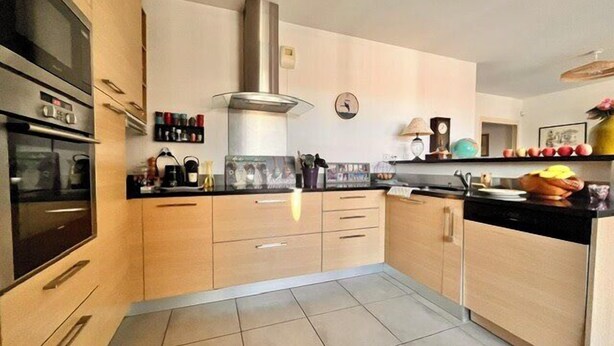 A modern kitchen with light wood cabinets, a stainless steel range hood, and a tiled floor. - Apart with loggia overlooking the canal, parking (La Rochelle)