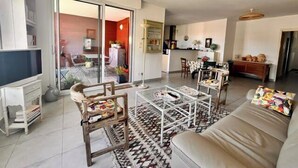 A living room with a sofa, coffee table, and chairs, a television, and a sliding glass door leading to a balcony. - Apart with loggia overlooking the canal, parking (La Rochelle)