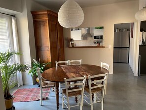 A dining area with a wooden table and white chairs, a kitchen with modern appliances, and a large wooden cabinet. - Charming large house in Velleron near Luberon. (Velleron)
