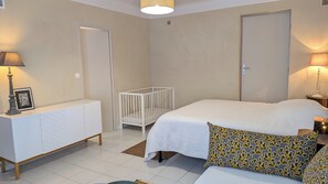 Une chambre à coucher avec un berceau, un lit, une table de chevet, une lampe et un tableau encadré posé sur une commode.