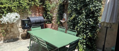 Un patio al aire libre con una mesa y sillas verdes, una parrilla y una planta en maceta.