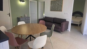 Ein Wohnzimmer mit einem runden Holztisch, einer Couch und einem Bett im angrenzenden Zimmer.