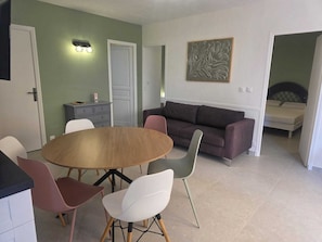 Ein Wohnzimmer mit einem runden Holztisch, einer Couch und einem Bett im angrenzenden Zimmer.