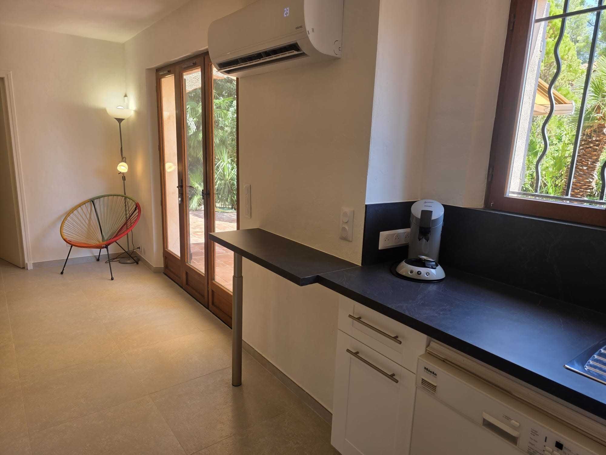 A kitchen with a black countertop, white cabinets, a red chair, and a window with a view of greenery.