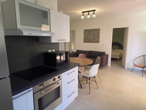 A modern kitchen with a built-in oven, a microwave, and a dining area with a table and chairs. - Family apartment near the calanques (Fréjus)