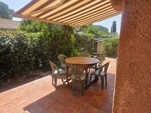 A covered patio with a round table and chairs, surrounded by greenery and a tiled floor. - Family apartment near the calanques (Fréjus)