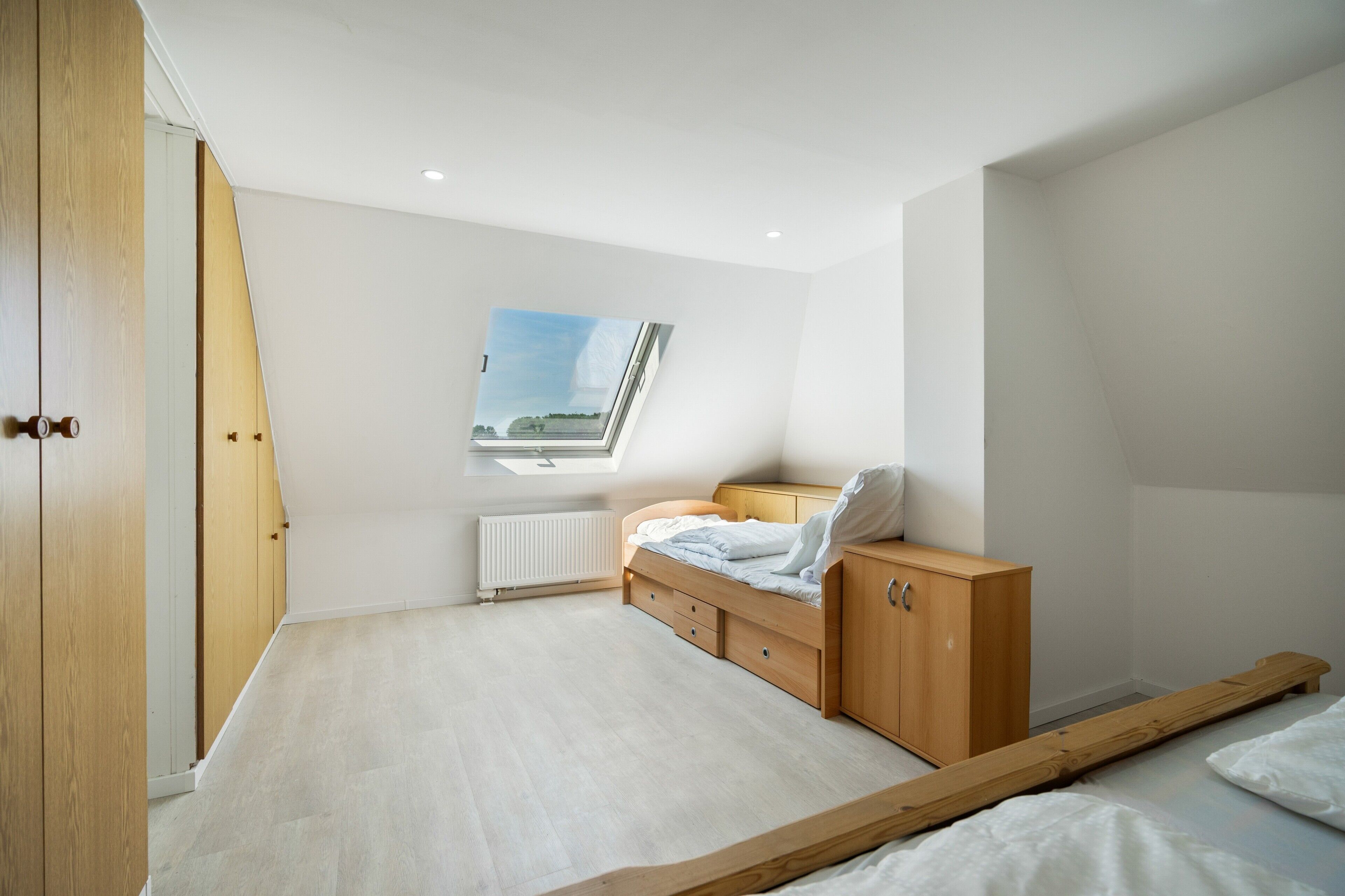Ein Schlafzimmer mit Dachfenster, einem Bett, einem Holzschrank und einer Heizung.