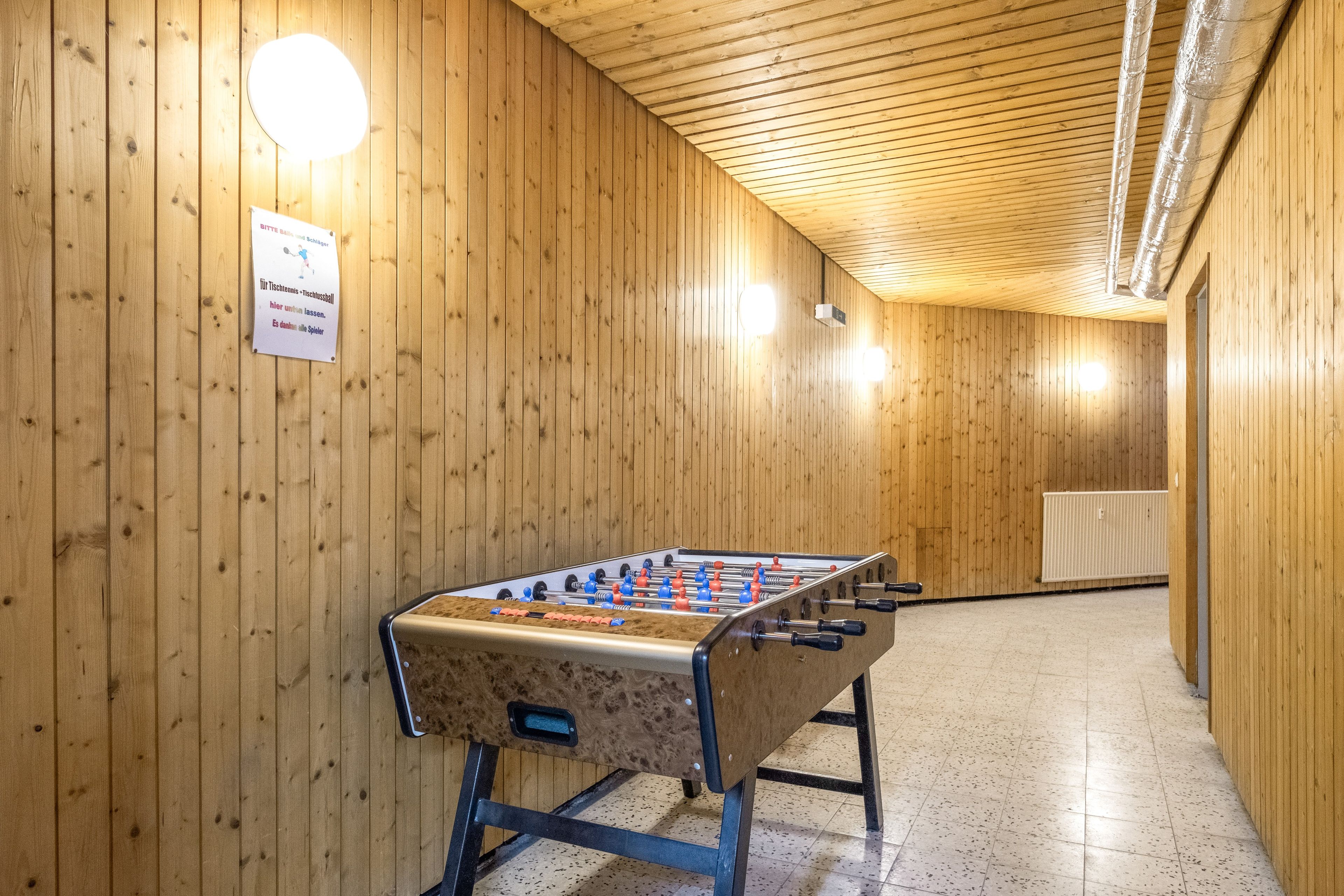 Een kamer met houten wanden, een tafelvoetbaltafel en een bord waarop staat dat de kamer voor tennis en tafeltennis is.