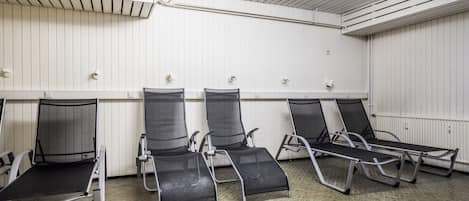A waiting area with four reclining chairs, a ceiling with ventilation, and a white wall with a radiator.