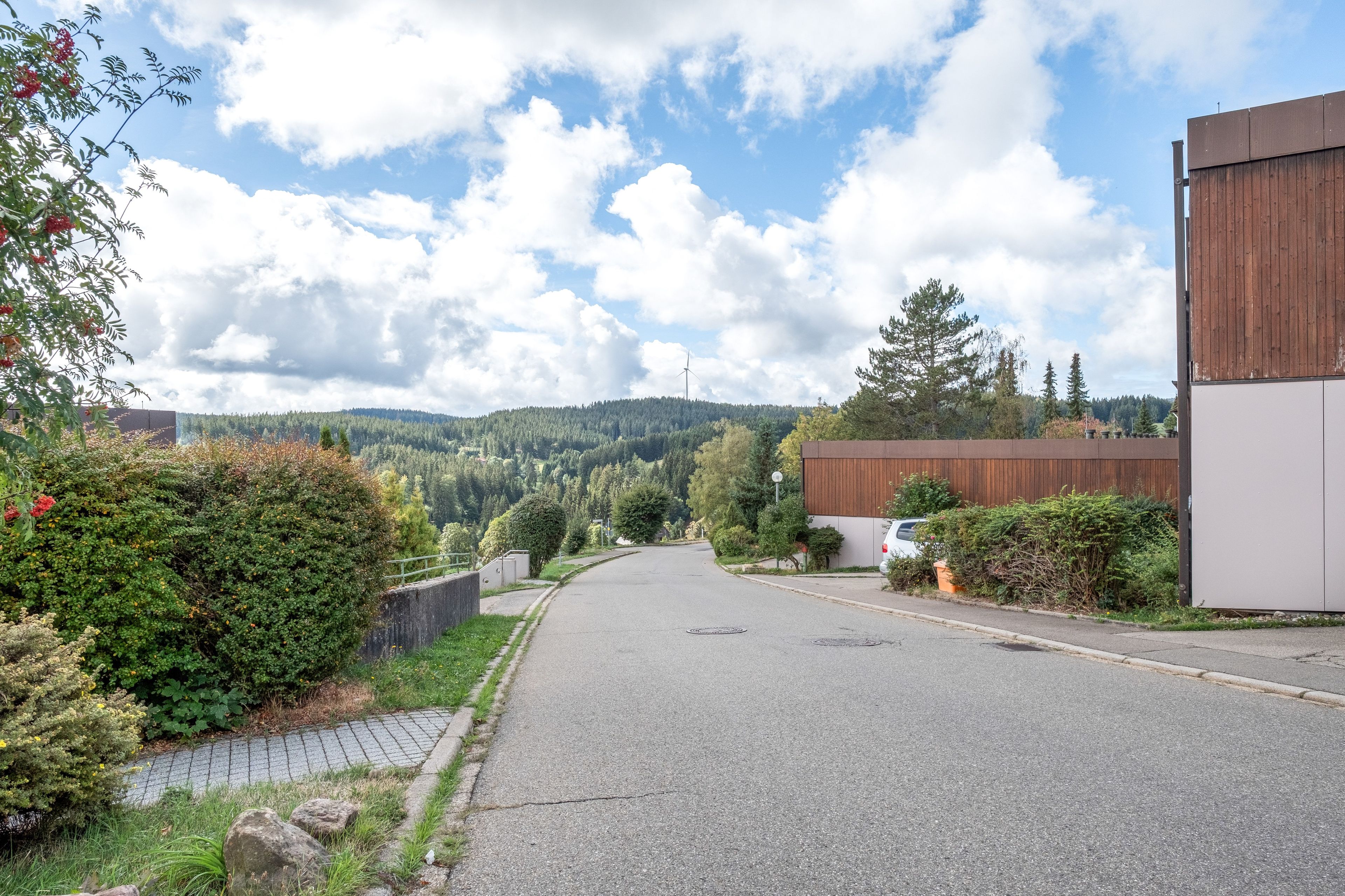 Eine Wohnstraße mit Häusern, einer asphaltierten Straße und einer hügeligen Landschaft im Hintergrund.