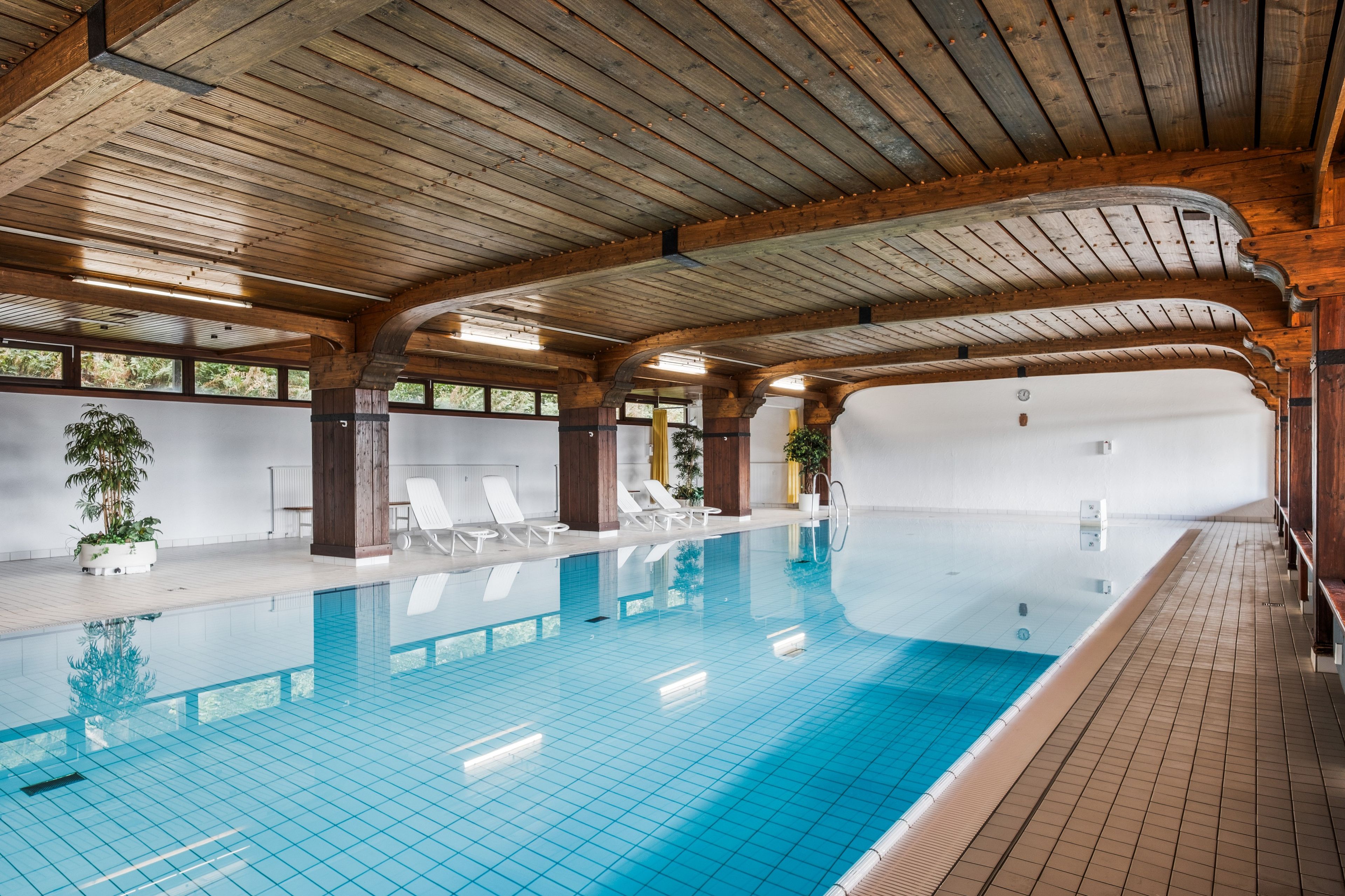 Ein Schwimmbad mit klarem, blauem Wasser, Holzbalken an der Decke und weißen Wänden.