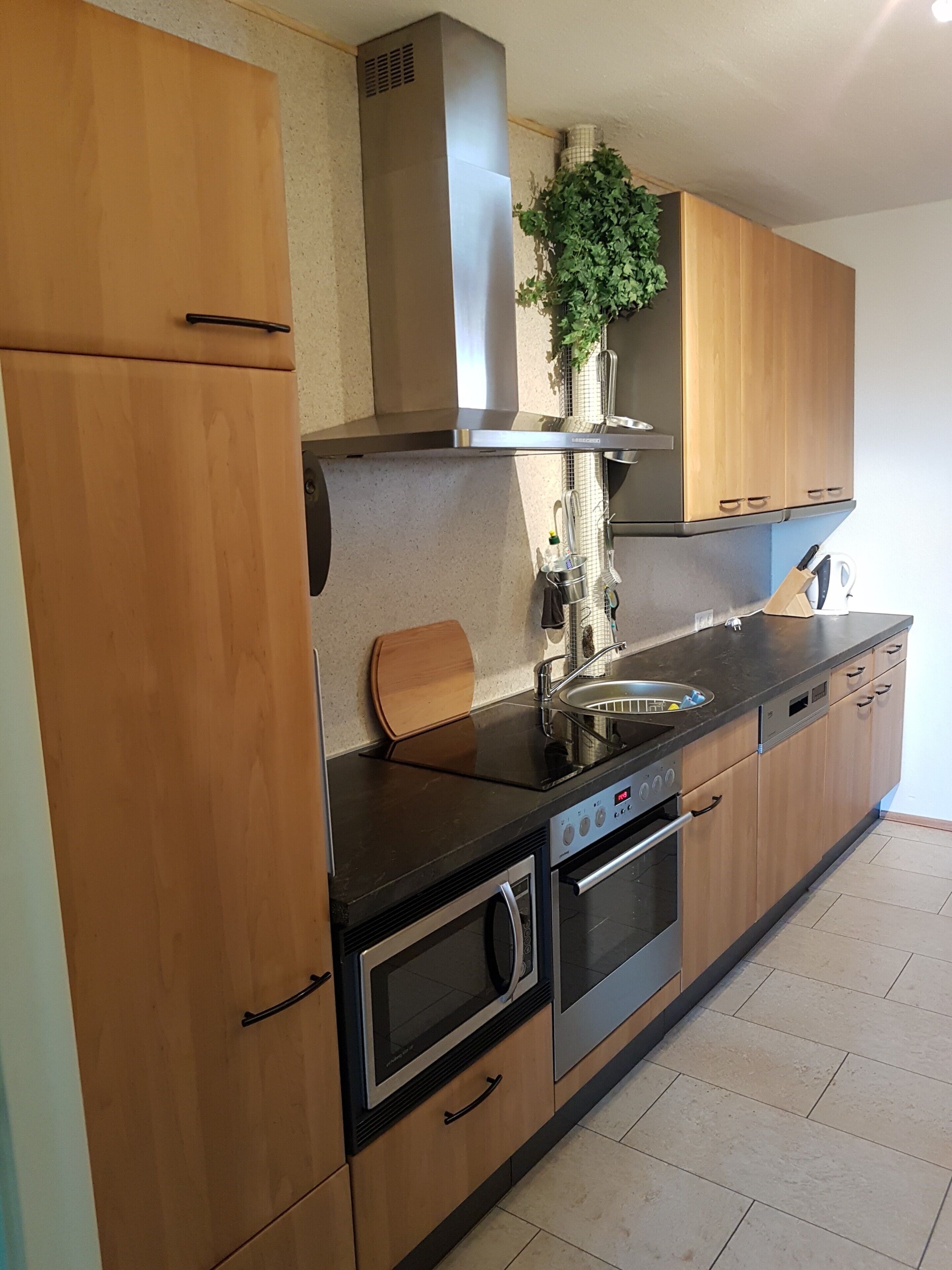 A modern kitchen with wooden cabinets, a stainless steel range hood, a built-in oven, and a microwave.