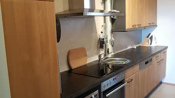 A modern kitchen with wooden cabinets, a stainless steel range hood, a built-in oven, and a microwave.