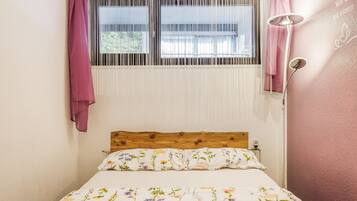 Une chambre à coucher avec une tête de lit en bois, une couvre-lit à motifs floraux et une fenêtre équipée de stores verticaux.