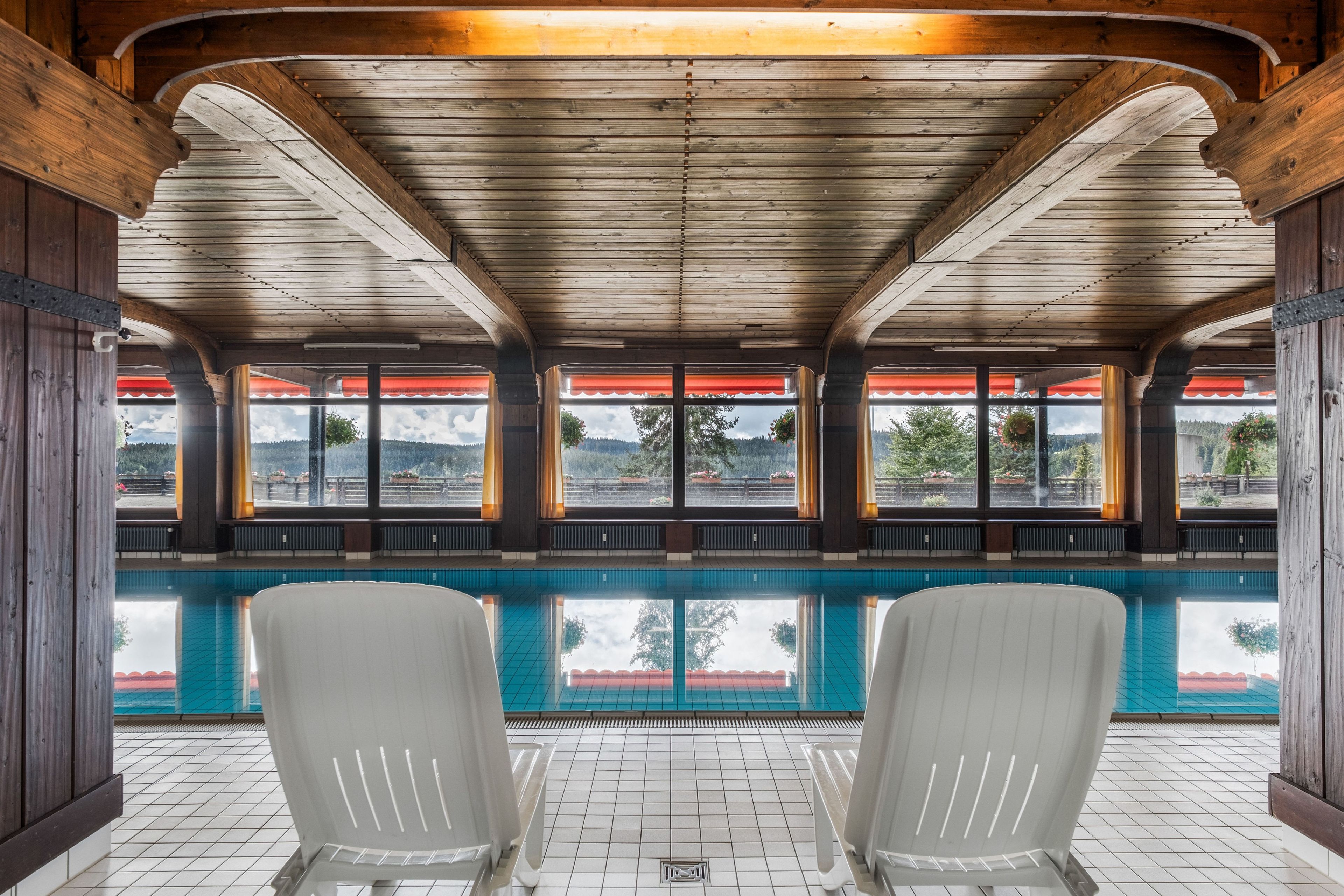 A pool area with wooden beams, a tiled floor, and two white chairs.