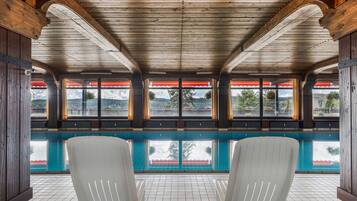 A pool area with wooden beams, a tiled floor, and two white chairs.
